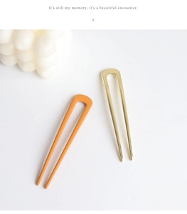 Detail of U-shaped hairpins in metallic gold and matte orange for elegant hairstyling