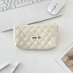 Macro view of beige quilted makeup bag with puppy label on a minimalist white desk