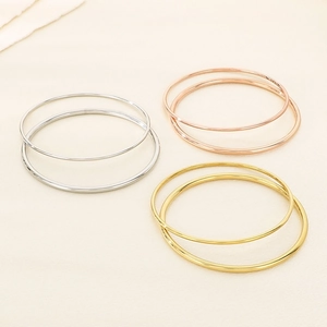Minimalist stainless steel bangles in silver, rose gold, and gold finishes on fabric