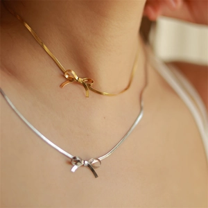 Close-up of dual-tone bow pendant necklaces with flat snake chains in 18K gold finish