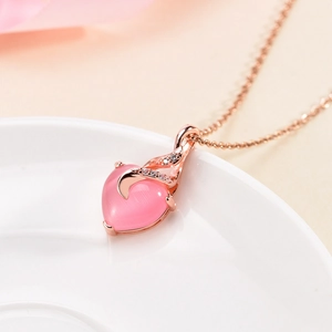Rose gold heart necklace with pink cat eye stone and zircon accents on a ceramic plate