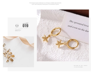 Detail of gold starfish pendant hoop earrings on textured white fabric background