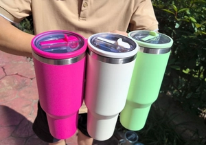Three colorful 40oz insulated stainless steel tumblers with handles held in outdoor setting