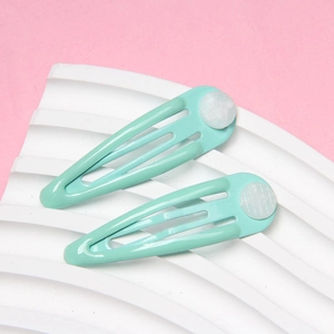 Detail showing two mint green metal snap hair clips on a white wavy texture base