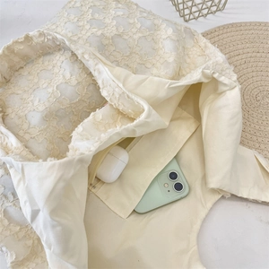Detail of the lace tote bag interior with a zipper pocket holding a phone and earbuds