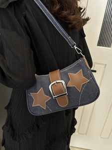Close-up of a blue denim shoulder bag featuring brown leather star patches and metal buckle