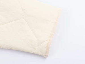 Detailed macro view of cream-white quilted waterproof fabric and fine stitching on jacket