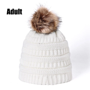 Detailed close-up of adult white knitted beanie with fluffy brown faux fur pom-pom