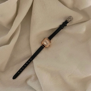 Close-up of a vintage square quartz watch with a black leather strap on a soft fabric base