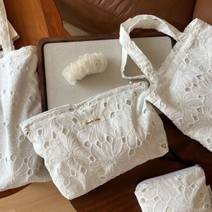 Close-up of white cotton lace tote bag with intricate floral embroidery and woven brand label