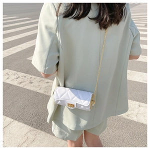 White quilted barrel crossbody bag with gold chain strap shown on model outdoors