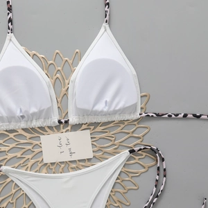 Flat lay of a white bikini set with pink leopard print ties on a gray background