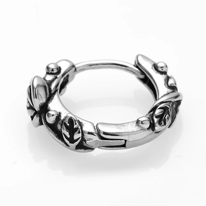 Macro shot of silver metal hoop earring featuring embossed leaf patterns and textured dots