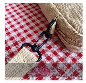 Detail shot of a black metal hook attached to a durable beige canvas crossbody bag strap