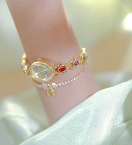 Detail showing a gold luxury watch with colorful gemstones on soft green silk fabric