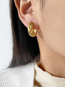 Detail of gold hoop earring with embossed celestial star moon patterns and tiny crystals
