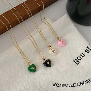 Close-up of four colorful enamel heart necklaces in green, black, white and pink on canvas