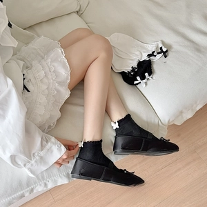 Close-up of black frilly ankle socks with white bows and black ballet flat shoes
