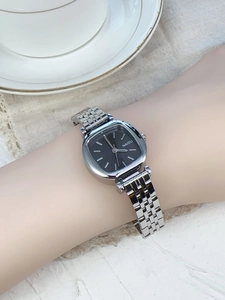 Silver steel strap square watch with black dial worn on wrist in a lifestyle setting
