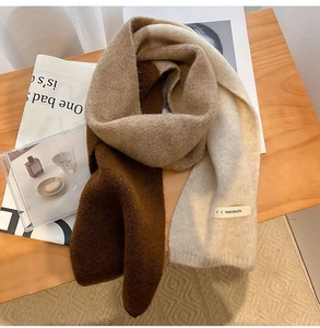 Detail of soft beige and dark brown knit scarf with a woven tag on a wooden table