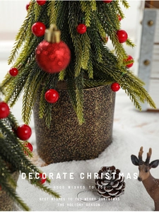 Close-up of mini snow-flocked Christmas tree with red berries in a gold-speckled pot