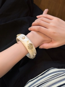 Detail of wide resin bangle with marble texture, golden shells and pearls on wrist
