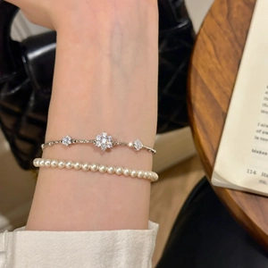 Detail of layered silver floral diamond bracelet and white round pearl bracelet on wrist