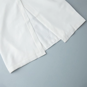 Detail of white sleeveless dress showing a side split hem and clean stitching