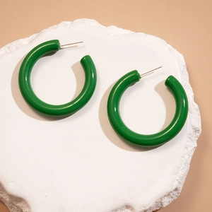 Gros plan de boucles d'oreilles en acrylique vert vif en forme de C sur un socle en pierre