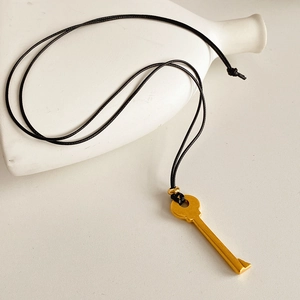 Gros plan détaillé du pendentif clé dorée avec cordon en cuir noir sur fond blanc épuré