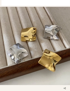 Detailed close-up of irregular wave metal earrings in gold and silver on a beige tray