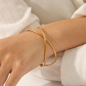 Minimalist 18k gold plated stainless steel crossover open bangle shown on a model's wrist