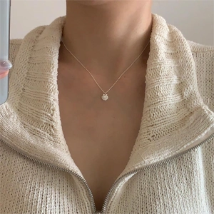Detail of shell pendant necklace on model wearing a beige knitted sweater