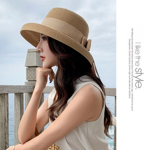 Detail view of a khaki sun straw hat with a side ribbon bow on a model at the beach