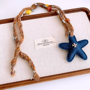 Dettaglio del ciondolo a stella in denim con croce in metallo su collana di perline