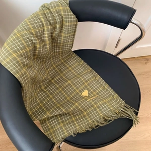 Detail of green and yellow plaid scarf featuring golden heart embroidery and fringes