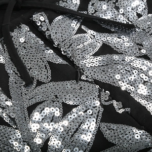 Détail de broderies florales à paillettes argentées sur tissu mesh noir de robe de soirée