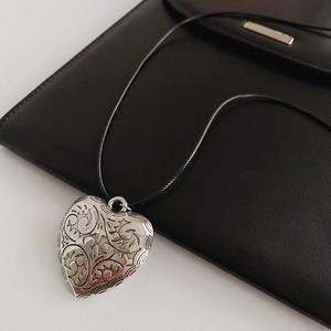 Macro detail of vintage heart pendant with ornate floral engraving on a black wax rope