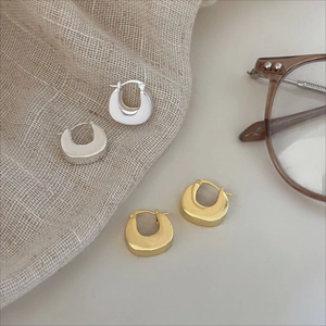 Close-up of chunky U-shaped gold and silver hoop earrings on soft linen fabric background