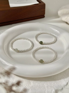 Detailed close-up of beaded pearl bracelets with green jade stones on a white ceramic plate