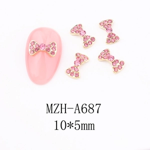 Detail view of 10x5mm gold bow nail charms with pink rhinestones on a manicure