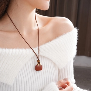 Close-up of brown leather pouch pendant with wooden beads and cords on a model