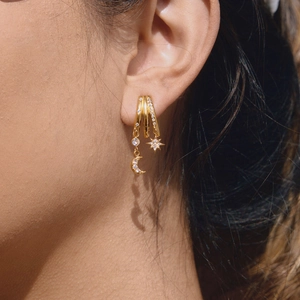 Détail de boucles d'oreilles dorées avec breloques étoile et lune serties de zircons