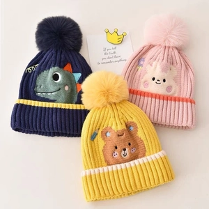 Detailed close-up of knitted baby beanies with cute animal patterns and large fluffy pom-poms