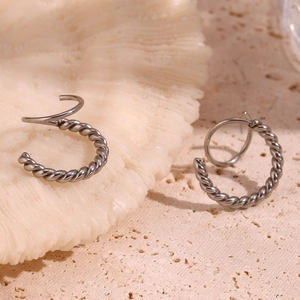 Detailed macro view of twisted silver-colored stainless steel earrings on a textured background