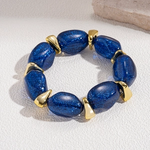 Close-up of blue acrylic beaded bracelet with gold spacers on white textured stone background
