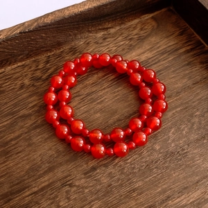 Detail of red agate beaded bracelet on a dark wood tray with natural polished finish