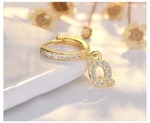 Macro shot of gold hoop earring with letter Q pendant and micro-pave white zircons