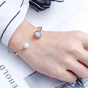 Close-up of rose gold bangle with blue crystal flower and pearl on a white surface