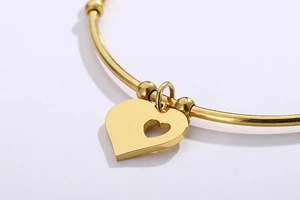 Detailed close-up of golden hollow heart charm and sleek metallic beads on a slim bangle